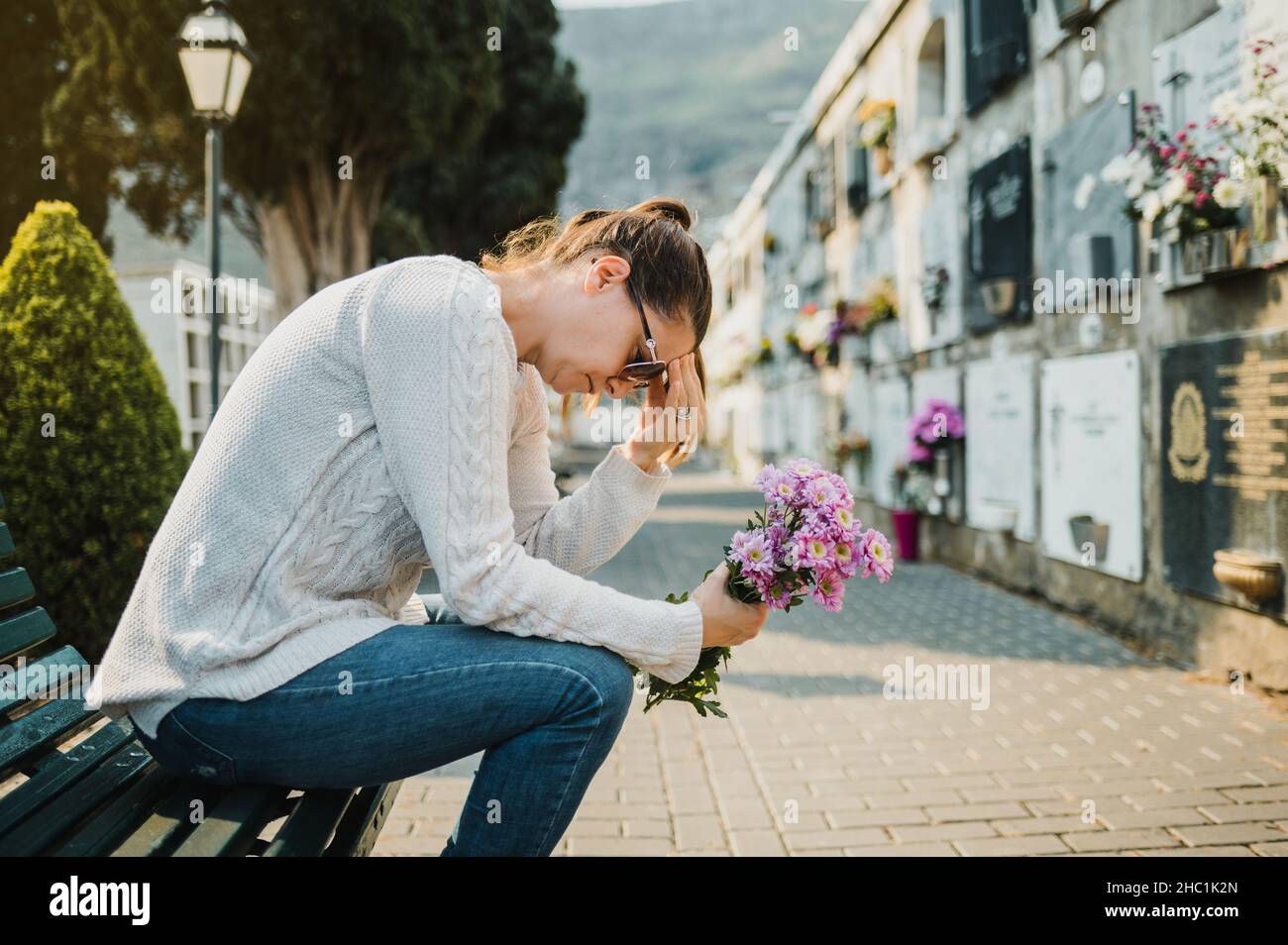 Triste femme pleure assise sur le banc avec des fleurs dans le cimetière Banque D'Images