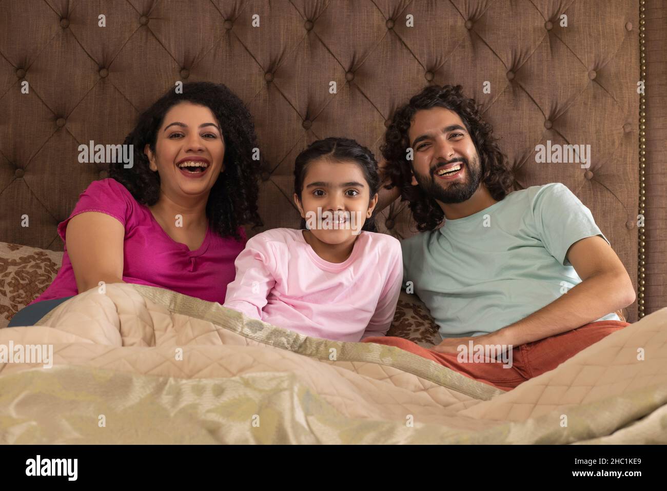 Parent avec leur fille regardant l'appareil photo et souriant ensemble dans la chambre Banque D'Images
