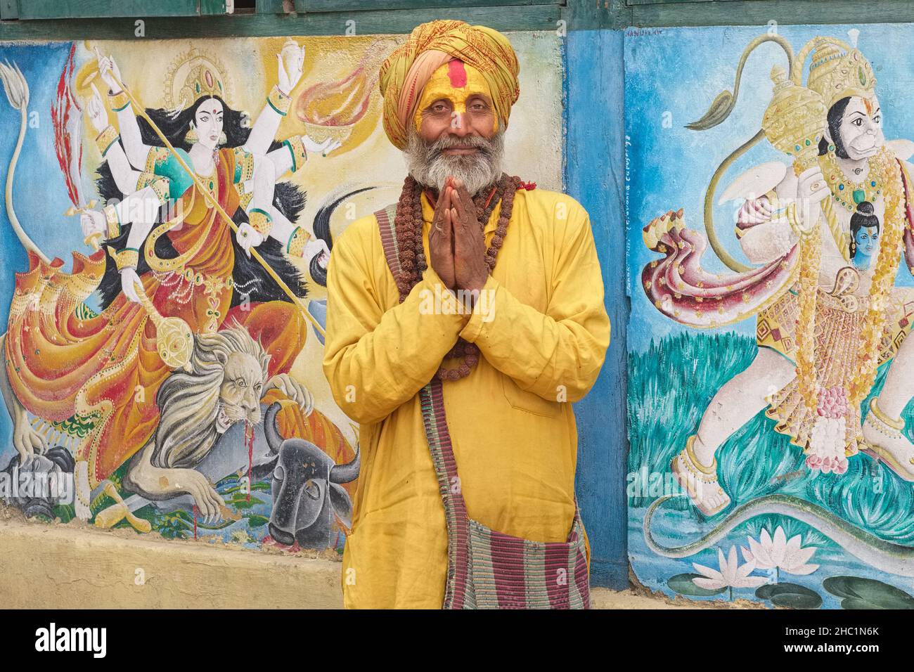 Un hindou sadhu (Saint-homme) qui exécute Namaste (salutation), Temple de Pashupatinath, Katmandou, Népal, entre les peintures murales de la déesse Durga et dieu singe Hanuman Banque D'Images