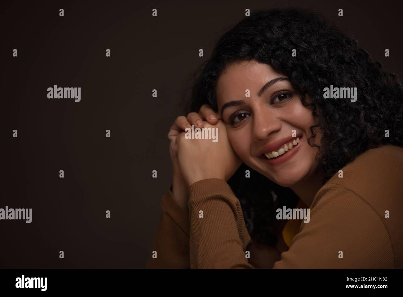 Femme adulte avec la tête penchée sur les deux mains regardant l'appareil photo et souriant Banque D'Images