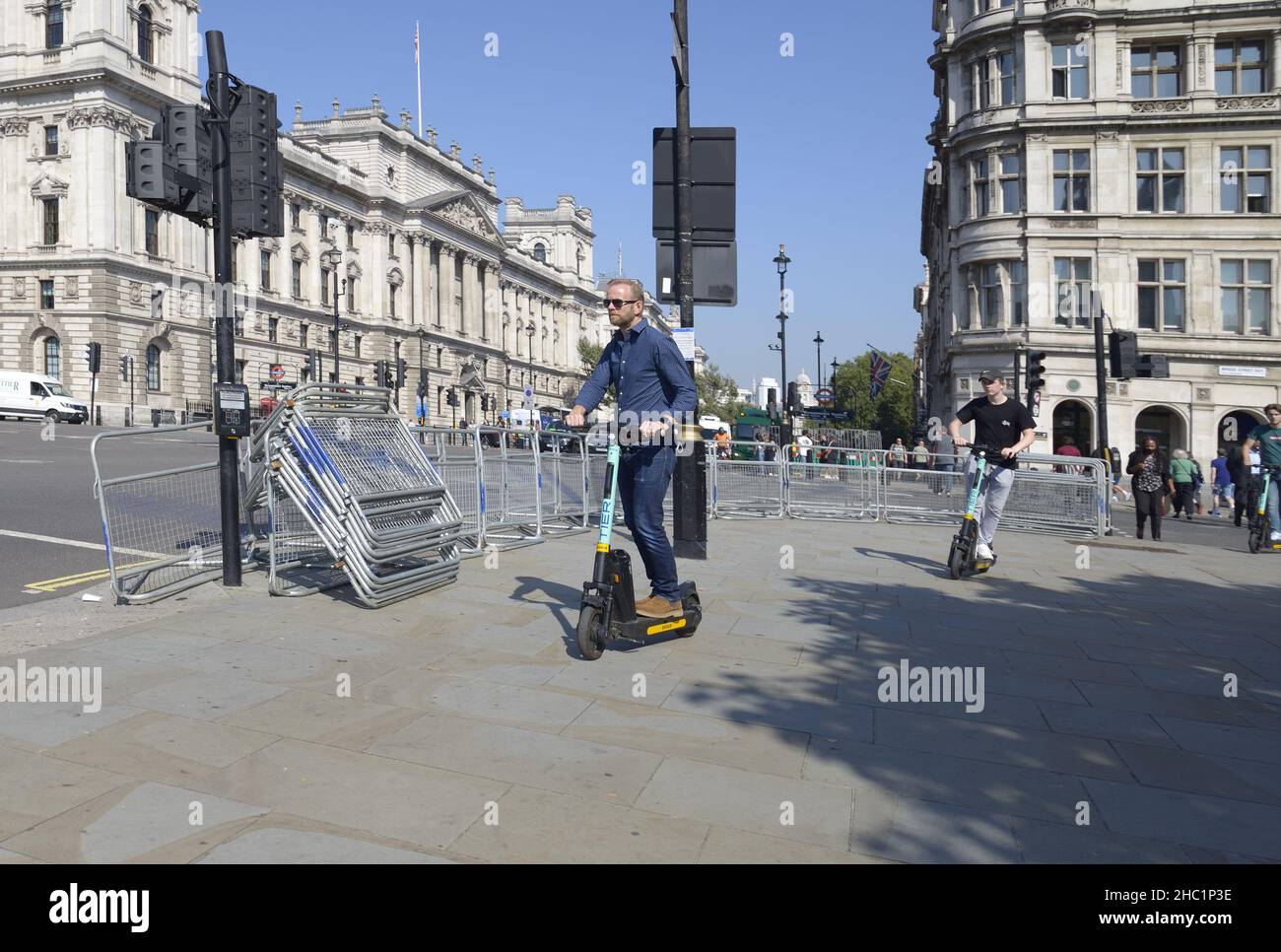 Londres, Angleterre, Royaume-Uni.Des hommes qui voyagent en e-trottinette sur le trottoir de la place du Parlement Banque D'Images