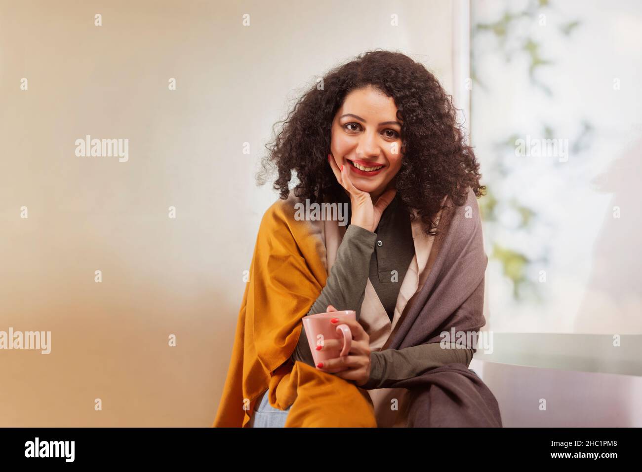 Bonne jeune femme adulte tenant une tasse de café près de la fenêtre dans le salon Banque D'Images