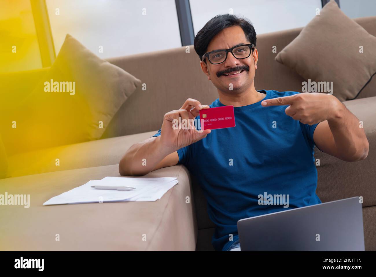 Homme d'âge moyen affichant une carte de crédit pendant les achats en ligne par ordinateur portable Banque D'Images