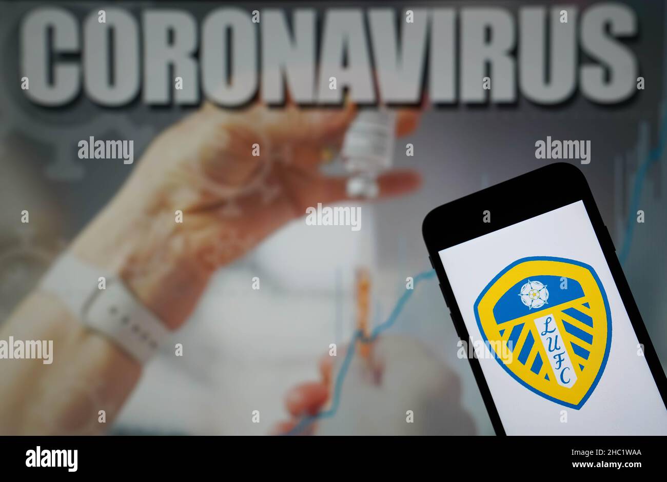 Photo du dossier datée du 09-01-2021 du logo Leeds United football Club affiché sur un téléphone portable avec une illustration du coronavirus sur un moniteur en arrière-plan.Le match de Liverpool contre Leeds et le match de Wolves contre Watford le lendemain de Noël ont été mis fin à cause d’infections à coronavirus, a annoncé la Premier League.Date d'émission : jeudi 23 décembre 2021. Banque D'Images