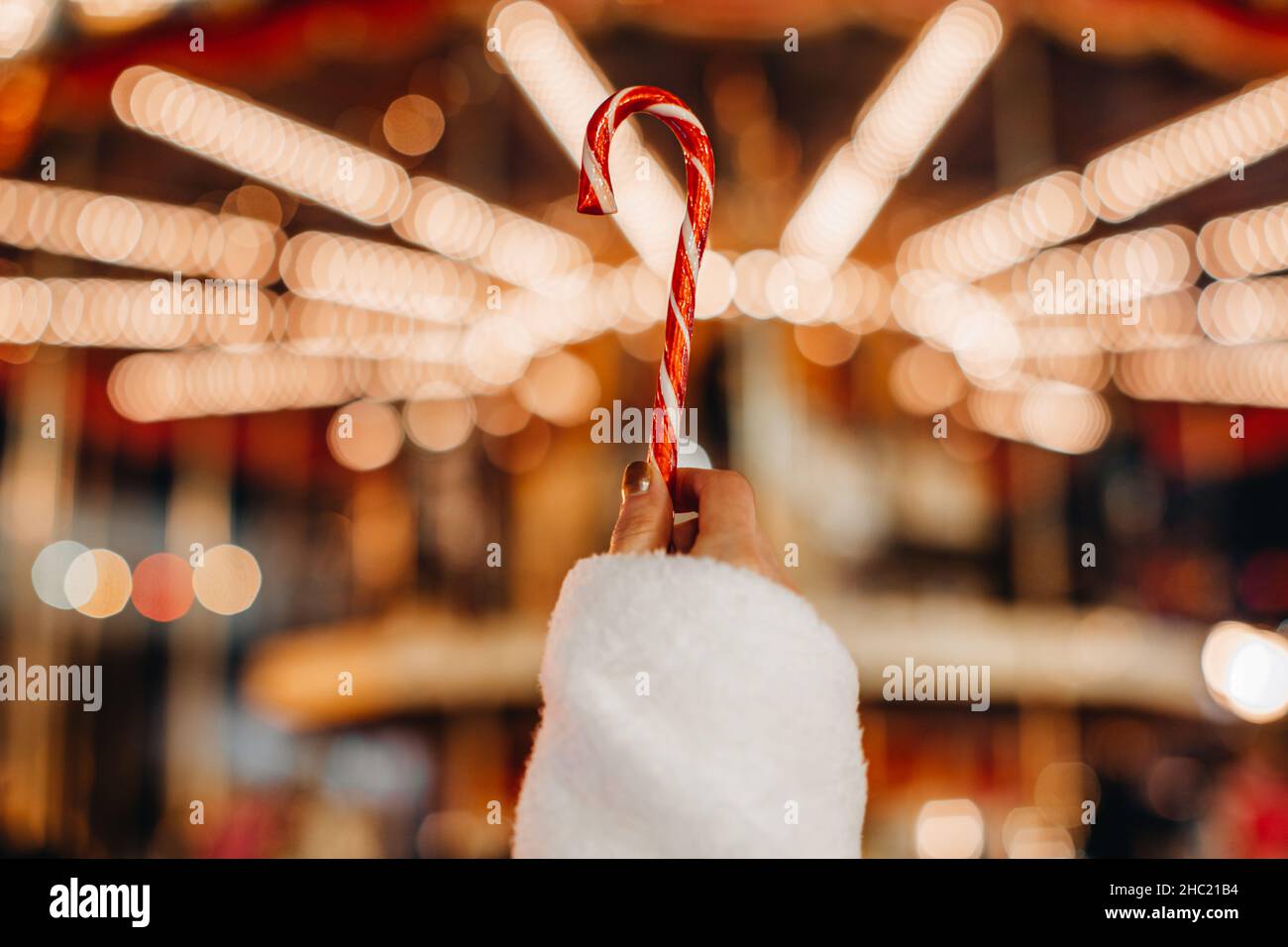 Mains de femmes tenant rouge blanc canne douce lollipop sur le fond des lumières de guirlande dorée.Détails magiques de Noël Banque D'Images