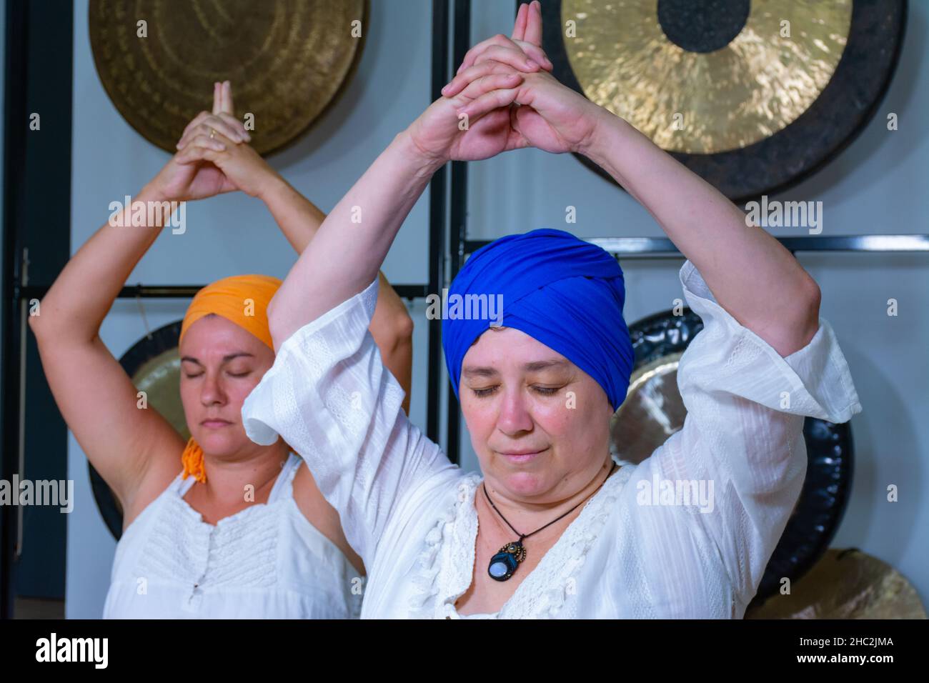 Deux femmes vêtues de blanc avec du turban pratiquant le yoga kundalini assis sur le sol avec leurs mains sur la tête Banque D'Images