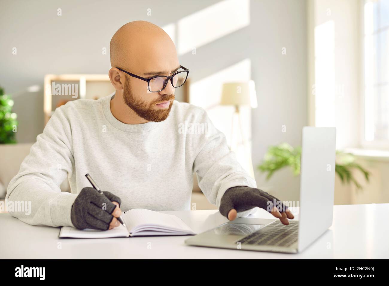 Homme en gants de compression pour soulager la douleur d'arthrite en utilisant l'ordinateur et l'écriture dans le bloc-notes Banque D'Images