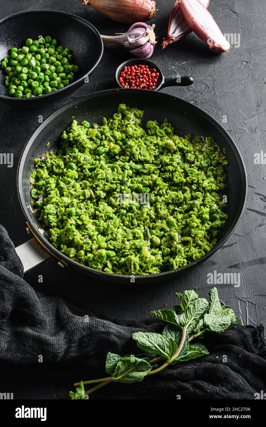 recette de petits pois anglais, poêle à frire cuite et petits pois dans un bol avec du poivre d'échalote à la menthe et du sel sur la surface de pierre noire, vue latérale de la nourriture de céto organique. Banque D'Images