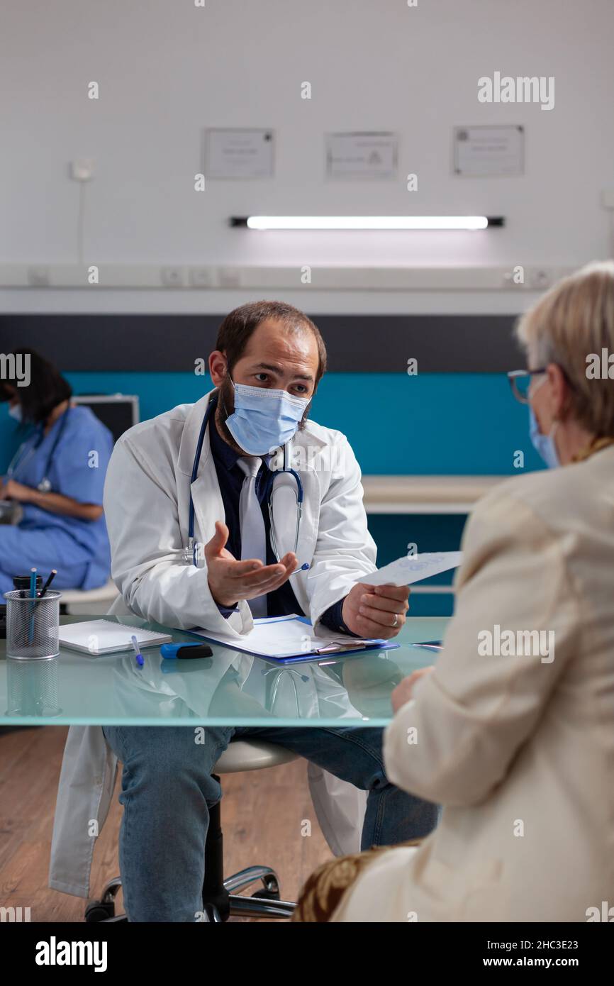 Médecin tenant un formulaire de prescription pour donner des médicaments à la femme mature pendant la pandémie de Covid 19.Médecin donnant le formulaire de contrôle après examen médical, donnant le traitement au pensionné. Banque D'Images