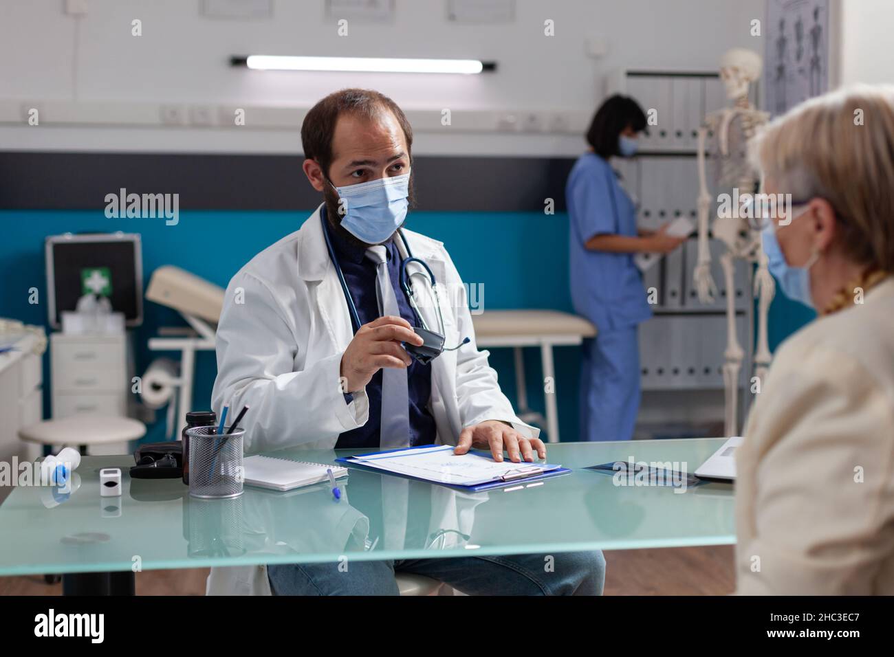 Medic avec masque facial utilisant le sceau médical sur le document de prescription, donnant des soins de santé à la femme aînée lors de la visite de contrôle.Un spécialiste appose le timbre sur le formulaire d'examen au bureau. Banque D'Images