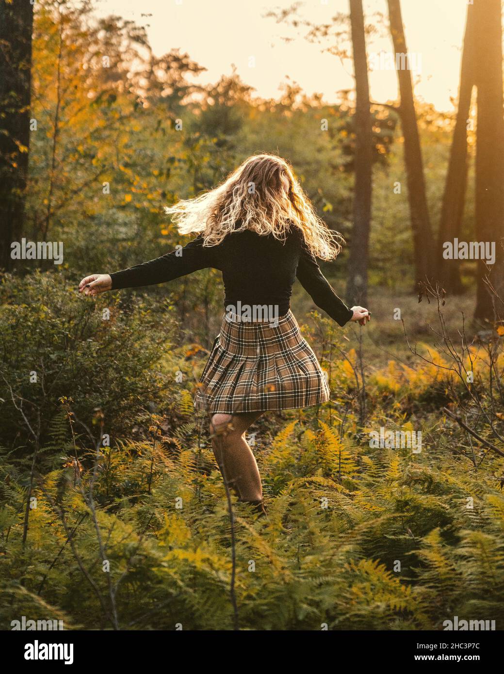 Jeune femme blonde danse volontiers dans la nature au coucher du soleil portant une manche longue noire et une jupe Banque D'Images