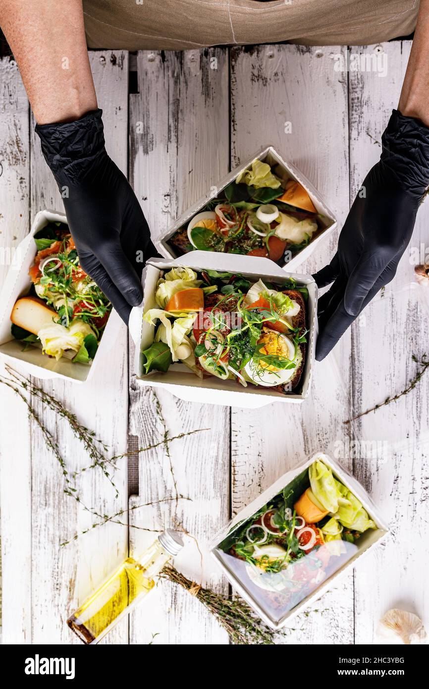 Les mains en gants noirs emballez un déjeuner d'affaires dans une boîte en carton.Concept de service de livraison de nourriture.Restaurant à emporter.Une cuisine délicieuse au travail Banque D'Images