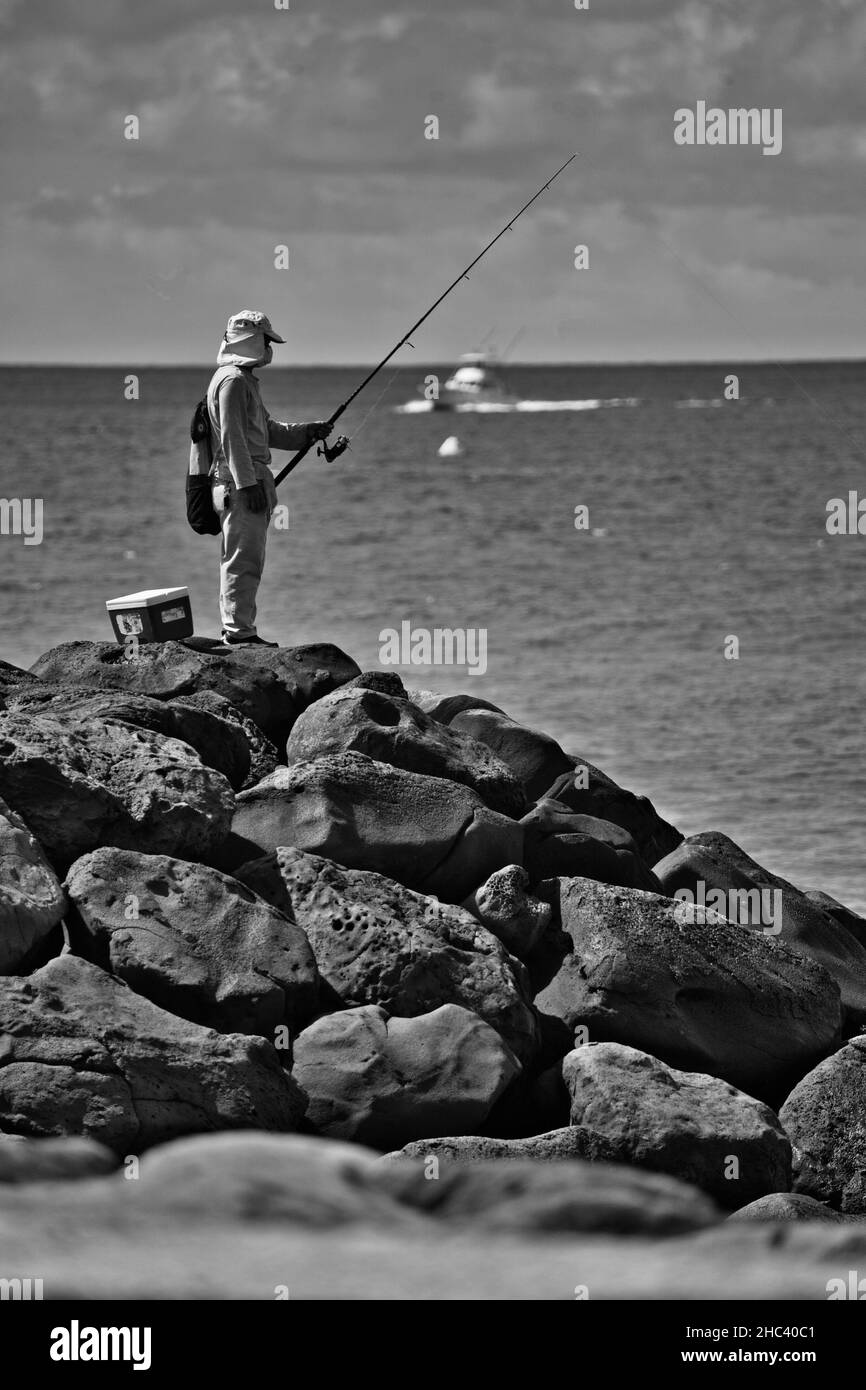 Plan vertical en niveaux de gris d'un pêcheur sur une colline rocheuse près de la mer Banque D'Images