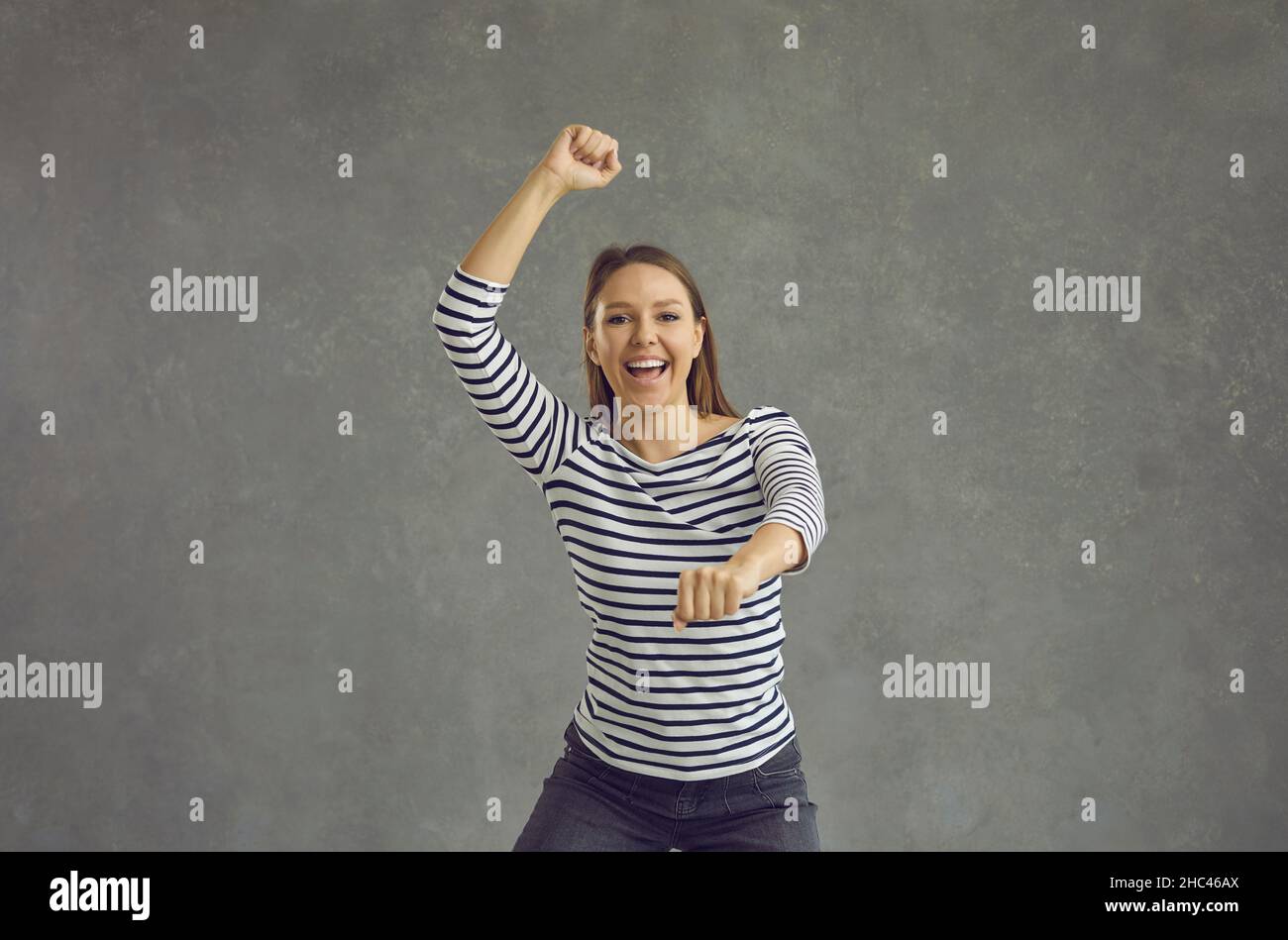 Une jeune femme ravie danse insouciante sur fond gris célébrant la victoire et le succès. Banque D'Images