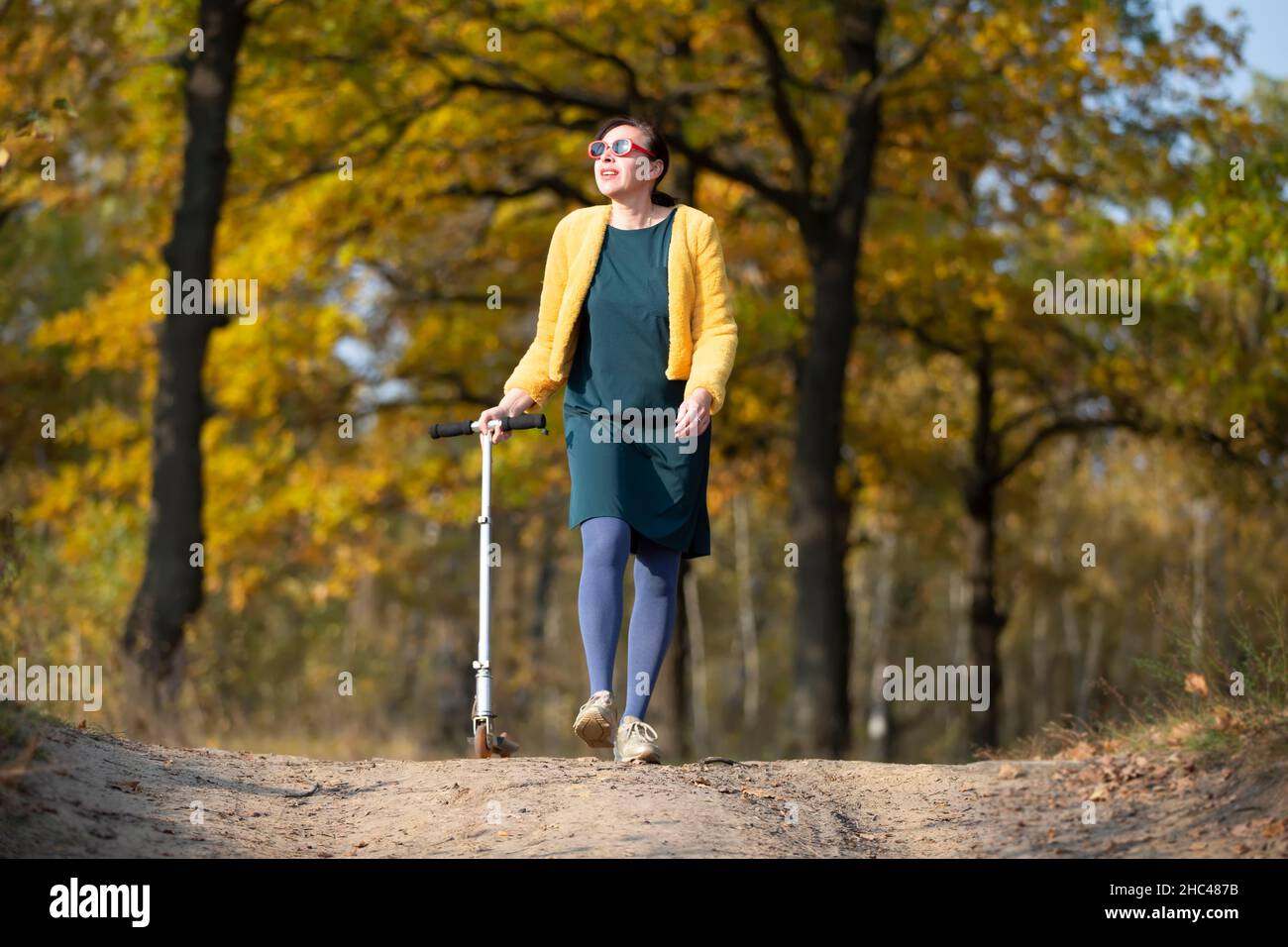 Une belle femme d'âge moyen marche avec un scooter en automne. Banque D'Images