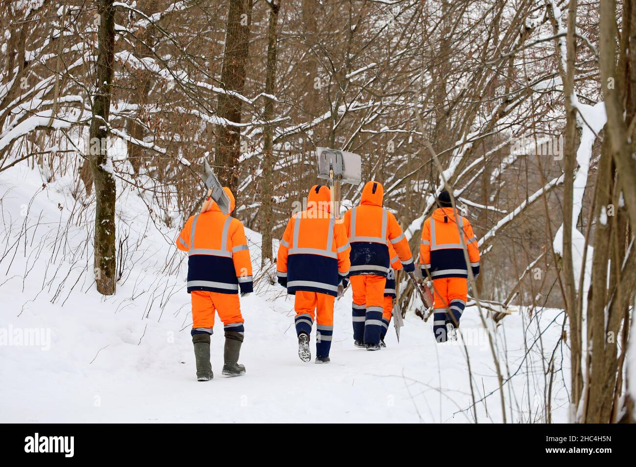 Les ouvriers en uniforme orange avec des pelles vont nettoyer la neige dans le parc.Nettoyage de rue dans la ville d'hiver Banque D'Images