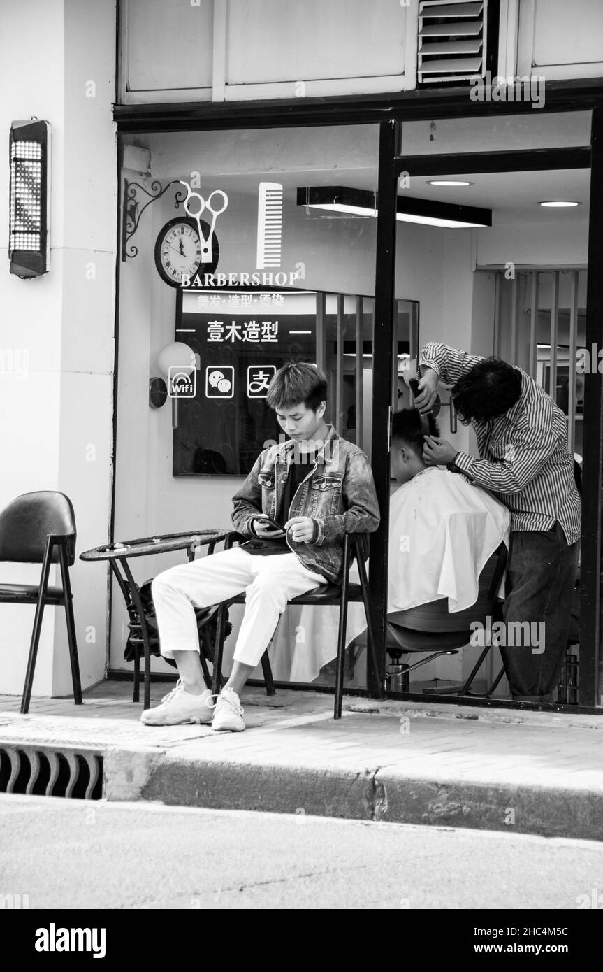Un barbershop dans les rues vers 1933 dans le district de Hongkou avec un jeune barbier dehors utilisant son téléphone.Shanghai, Chine. Banque D'Images