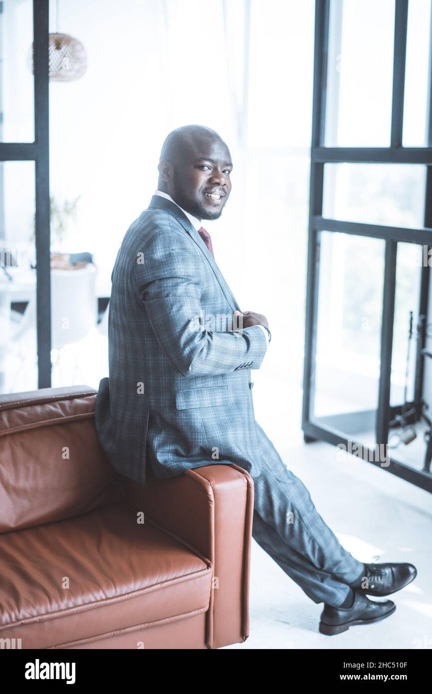 Homme d'affaires de 30s dans un costume classique à carreaux gris se trouve sur l'arrière du canapé dans son salon.Il se tourne pour regarder par-dessus son épaule à la caméra .Gros plan.Copier l'espace.Photo de haute qualité Banque D'Images