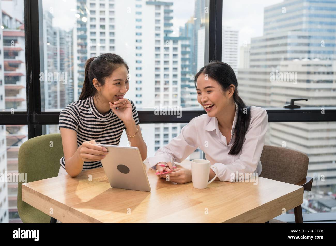 Deux employées asiatiques s'amusent à parler et à montrer une tablette sur un bureau moderne Banque D'Images