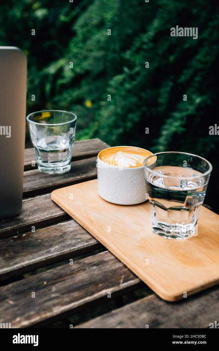 Plan vertical de deux verres d'eau et d'une tasse de café latte sur une table en bois devant un arbre Banque D'Images