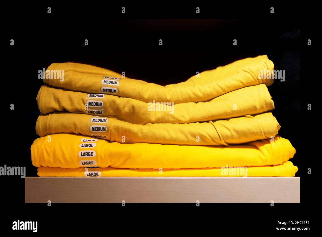 Gros plan d'une pile de t-shirts jaunes avec de grands et moyens autocollants isolés sur fond noir Banque D'Images
