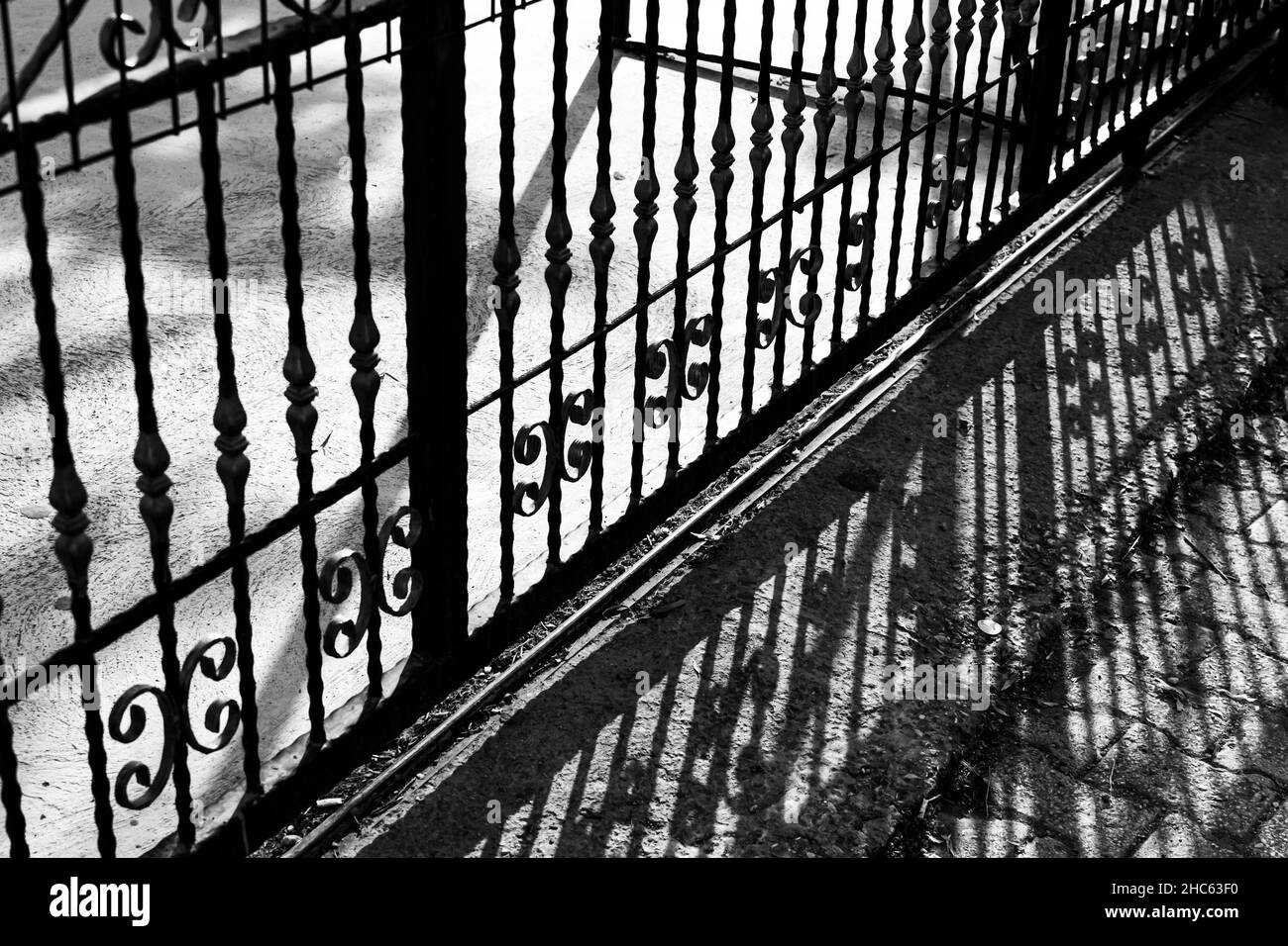 Photo en niveaux de gris d'une clôture en métal avec ombre sur le sol par une journée ensoleillée Banque D'Images