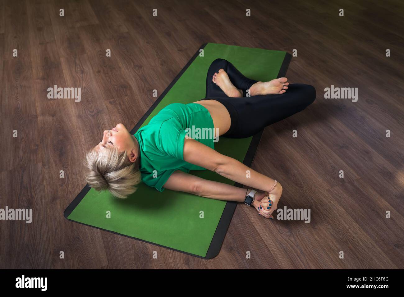 Une femme pratiquant le yoga, faisant l'exercice Eka bhuja swastikasana en pamasana, le bien-être pose sur l'épaule, allongé sur un tapis dans le studio, l'exercice Banque D'Images