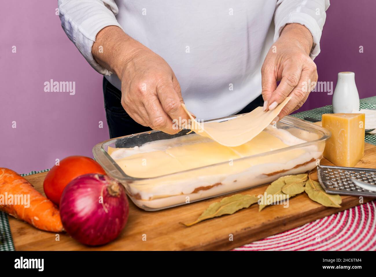 Mains d'une femme méconnaissable qui fait de la lasagne dans un plateau en verre avec des ingrédients crus autour. Banque D'Images