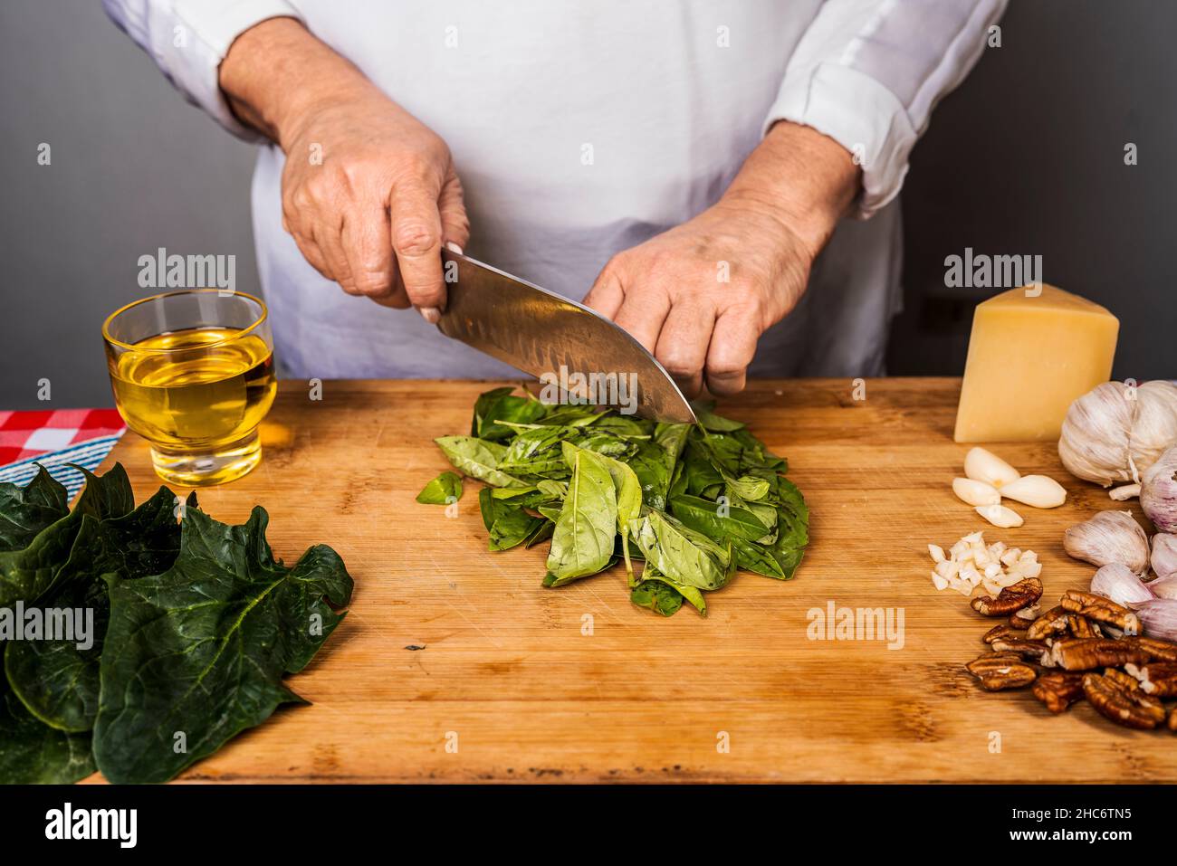 Vue de face d'une femme adulte méconnue coupant du basilic avec un couteau de cuisine sur une table en bois pour la préparation d'une sauce pesto. Banque D'Images