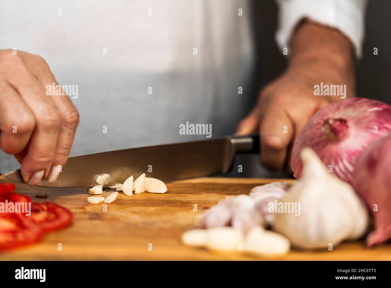 Vue rapprochée d'une femme adulte méconnue utilisant les deux mains sur un couteau de cuisine pour hacher un ail sur une planche à découper pour la préparation de lasagnes. Banque D'Images