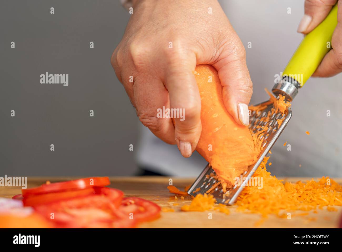 Vue rapprochée des mains d'une femme adulte qui râpe une carotte avec une râpe sur un panneau en bois pour la préparation de lasagnes avec espace de copie. Banque D'Images