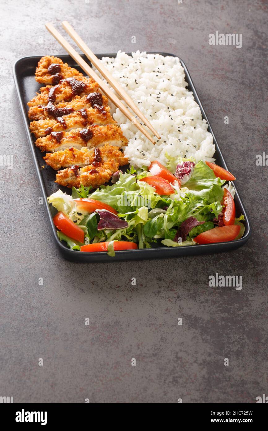 Le katsu de poulet est un plat traditionnel japonais servi avec de la salade de riz et de légumes dans l'assiette sur la table.Verticale Banque D'Images
