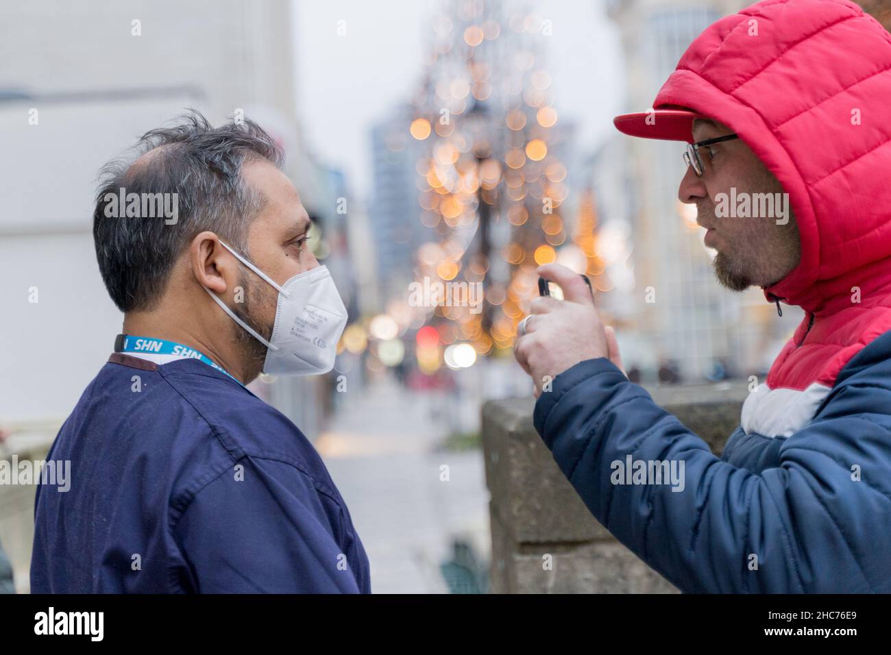 Londres Royaume-Uni 25December 2021.Le personnel de NSH explique à anti-vaxer dans le sweat à capuche rouge au sujet de la vaccination.Le personnel du NHS et les bénévoles de la communauté passent leur jour de Noël à l'hôtel de ville de Redbridge, offrant le vaccin contre le coronavirus, jingle jab pour toutes les personnes éligibles comme le meilleur cadeau de Noël de son genre, en maintenant tout le monde en sécurité car les cas d'Omicron sont trouvés doubler tous les deux jours.Credit: Xiu Bao/Alamy Live News Banque D'Images