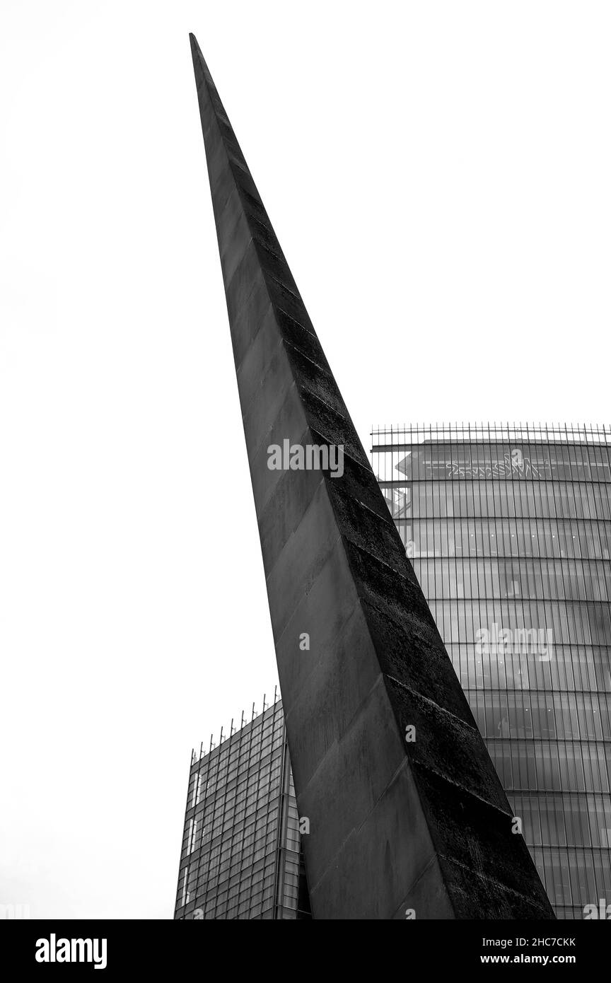 Photo monochrome verticale à faible angle d'un monument en forme de triangle avec arrière-plan d'un bâtiment vitreux Banque D'Images