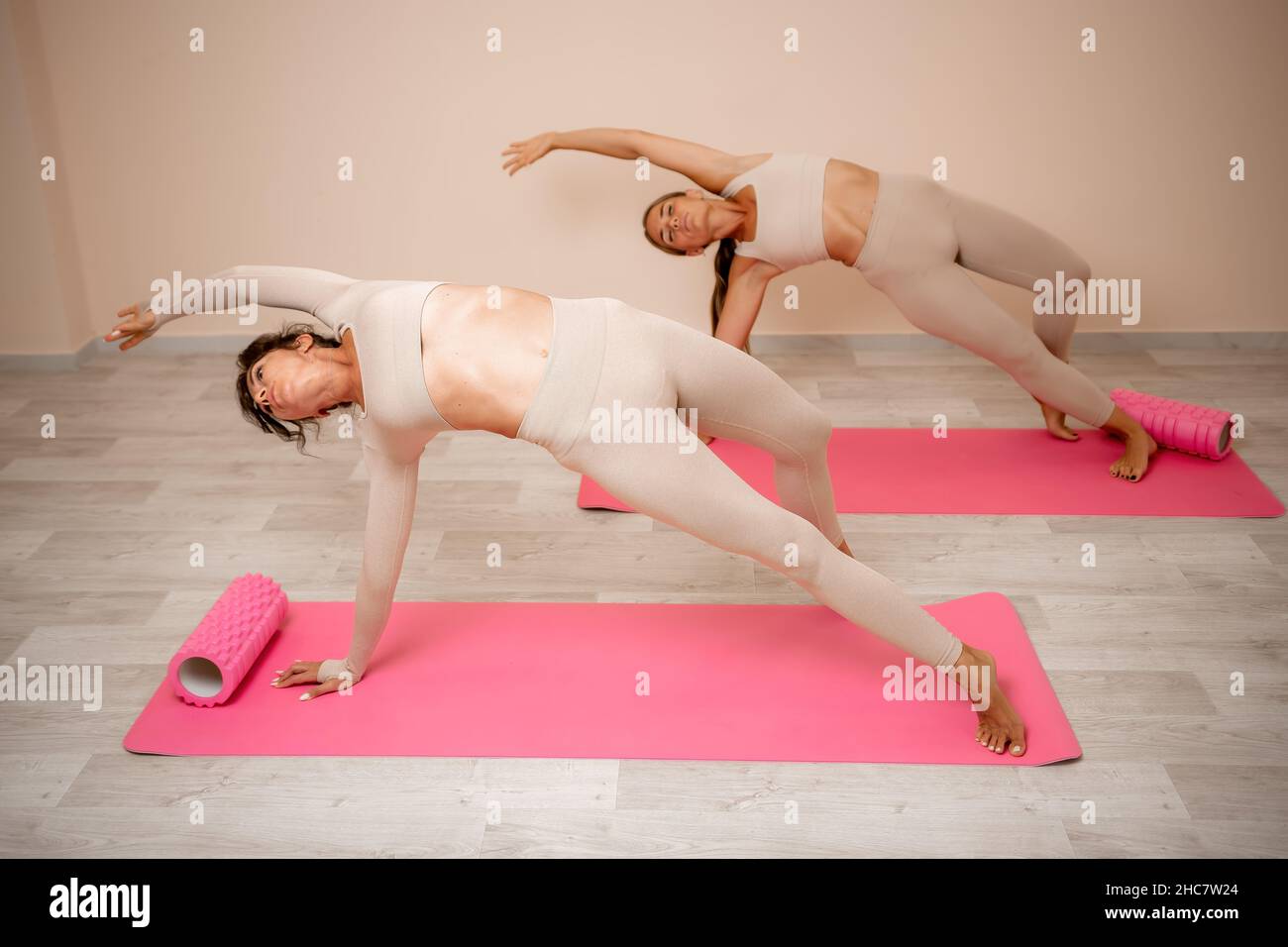 Les femmes d'âge moyen sont bien à la recherche, un instructeur de fitness  en vêtements de sport beige, se préparant à s'étirer et à se pilates sur un  tapis de yoga dans