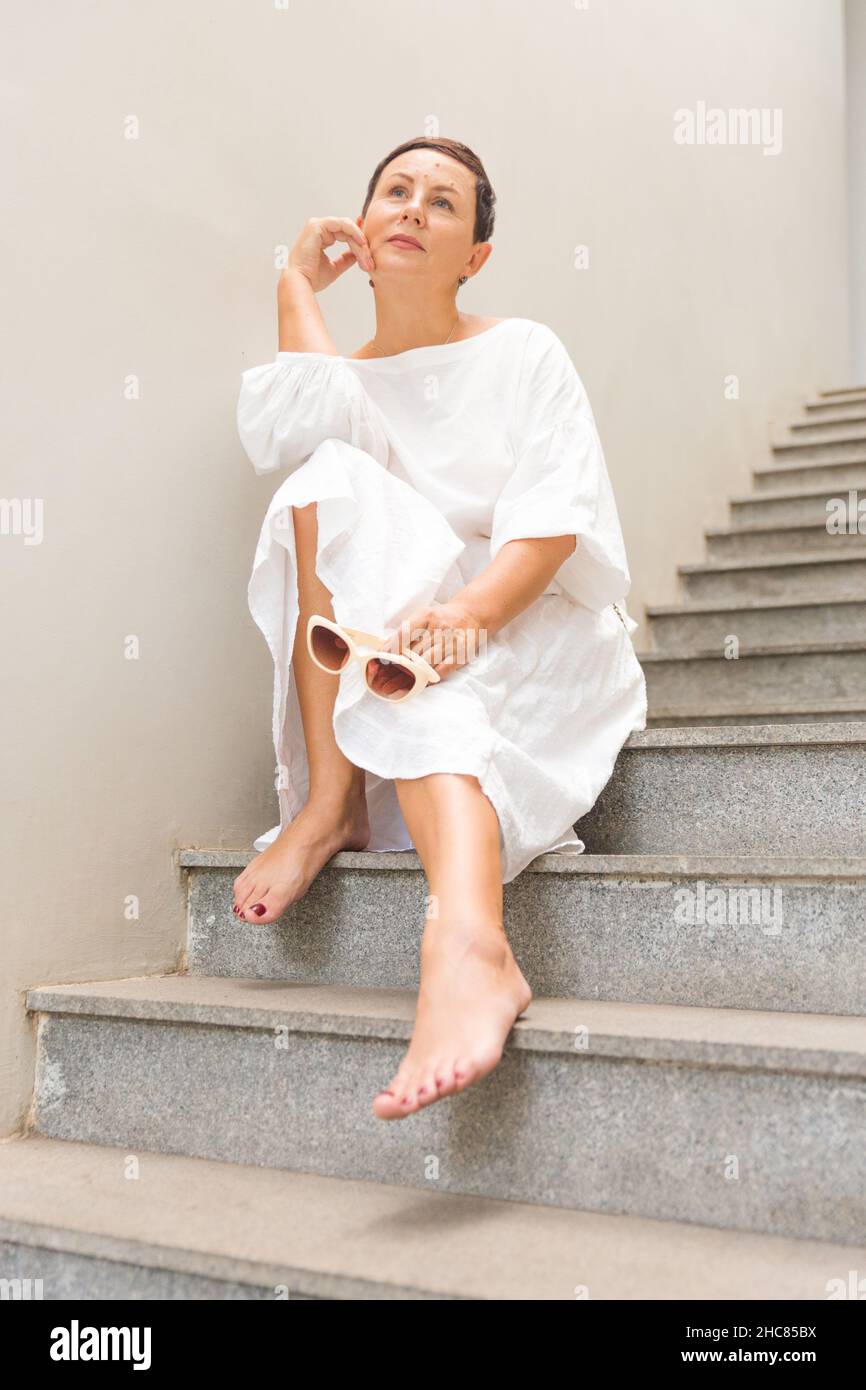 Belle femme d'affaires à la mode souriante assise sur les escaliers et posant. Banque D'Images