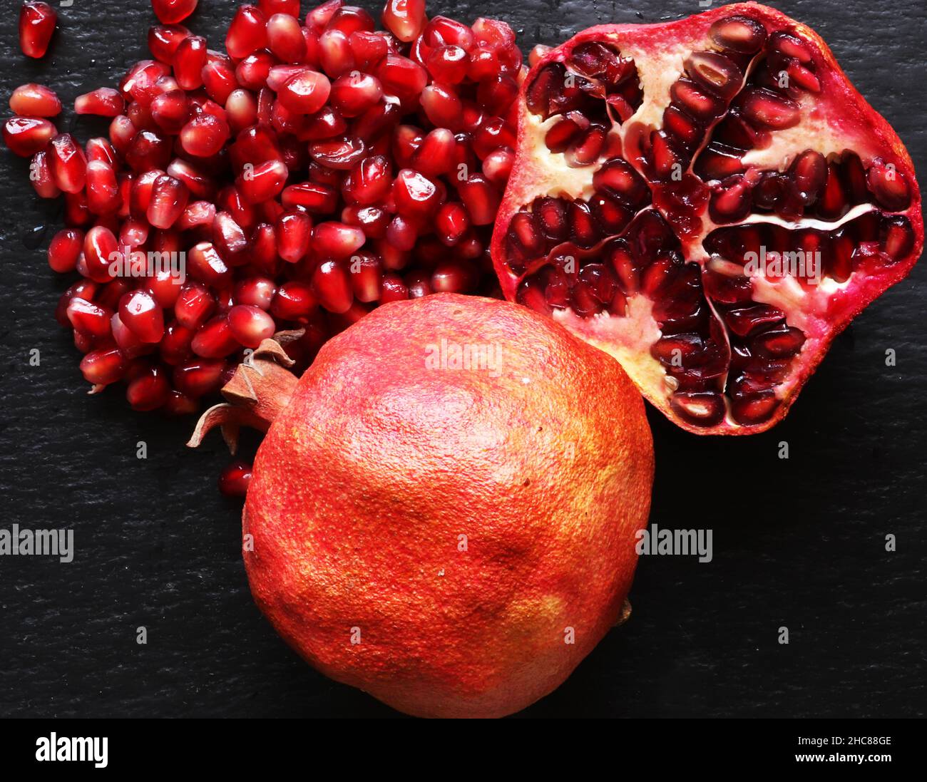 Macro photographie de deux grenades organiques un tout et l'autre coupé en deux avec ses graines sur fond d'ardoise pour les illustrations alimentaires Banque D'Images