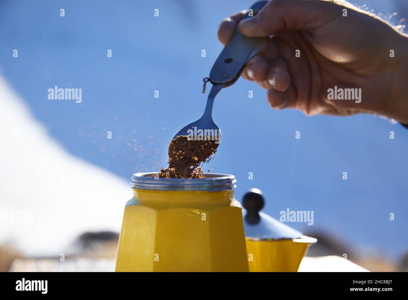 Homme randonneur qui fait du café de près depuis le pot de moka jaune en plein air dans les montagnes d'hiver enneigées.Vieux style café pot vintage camping extérieur Banque D'Images