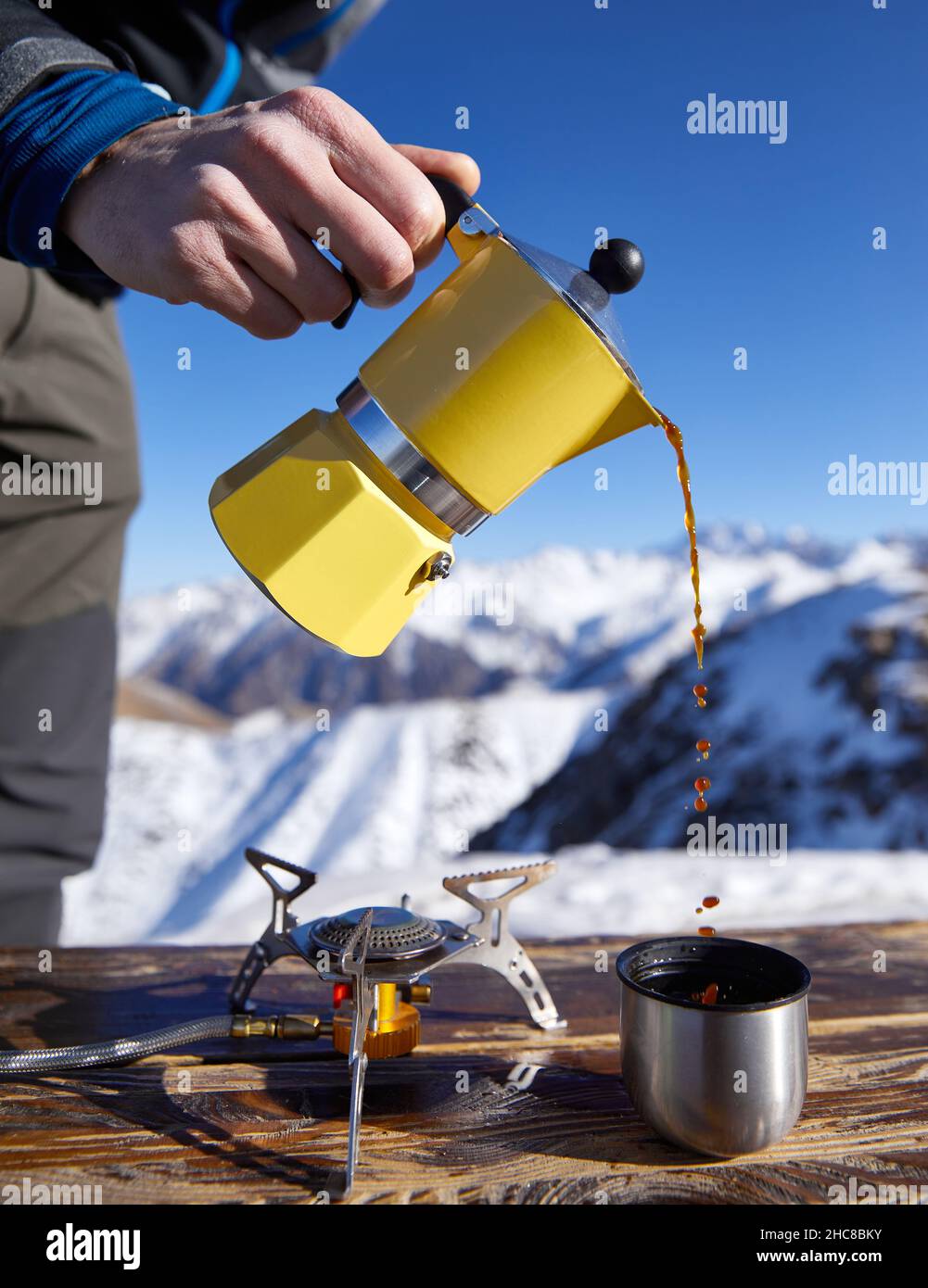 Homme randonneur versant du café de Moka jaune pot à l'extérieur dans la neige hiver montagnes.Vieux style café pot vintage camping extérieur Banque D'Images