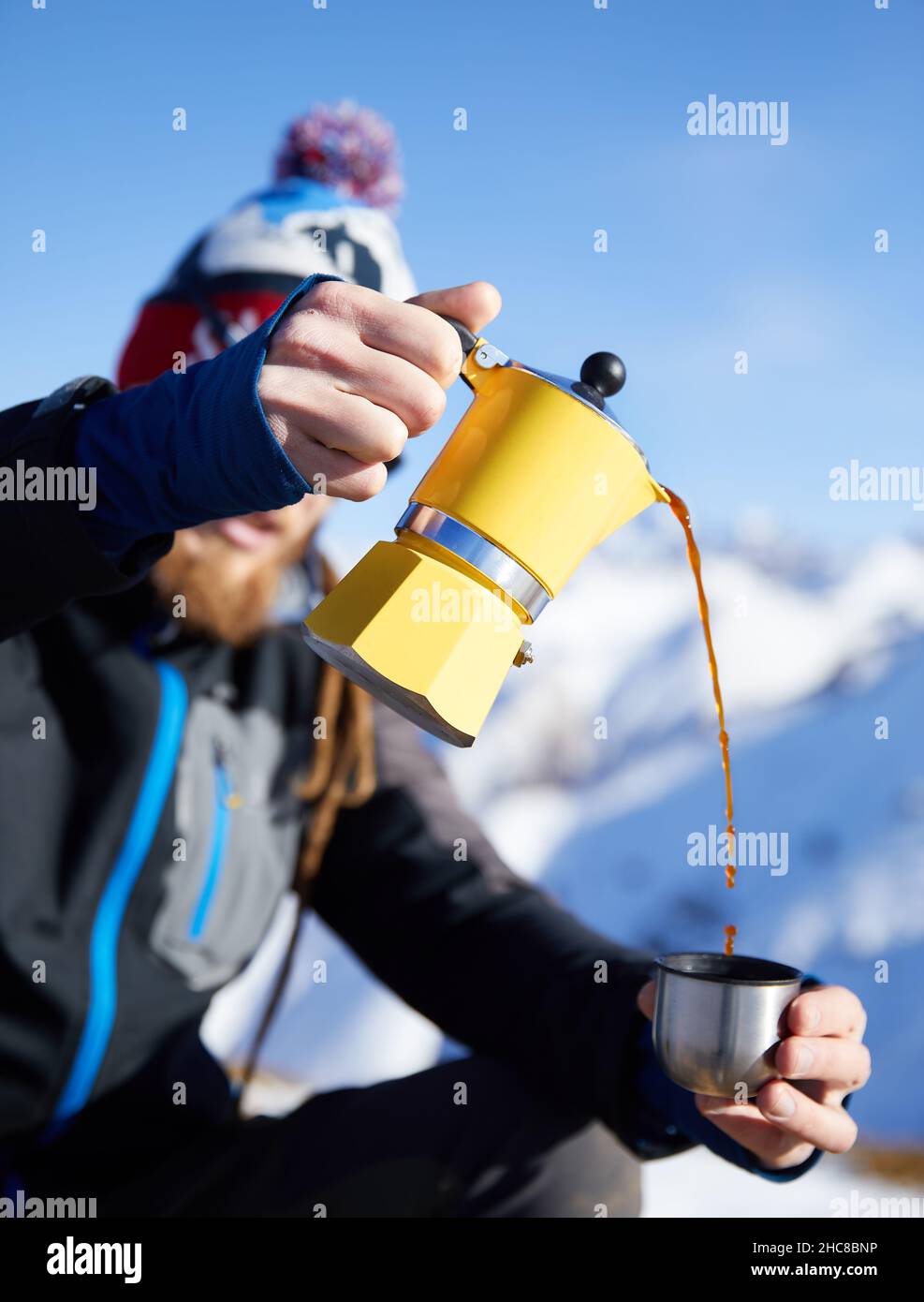 Homme randonneur versant du café de Moka jaune pot à l'extérieur dans la neige hiver montagnes.Vieux style café pot vintage camping extérieur Banque D'Images