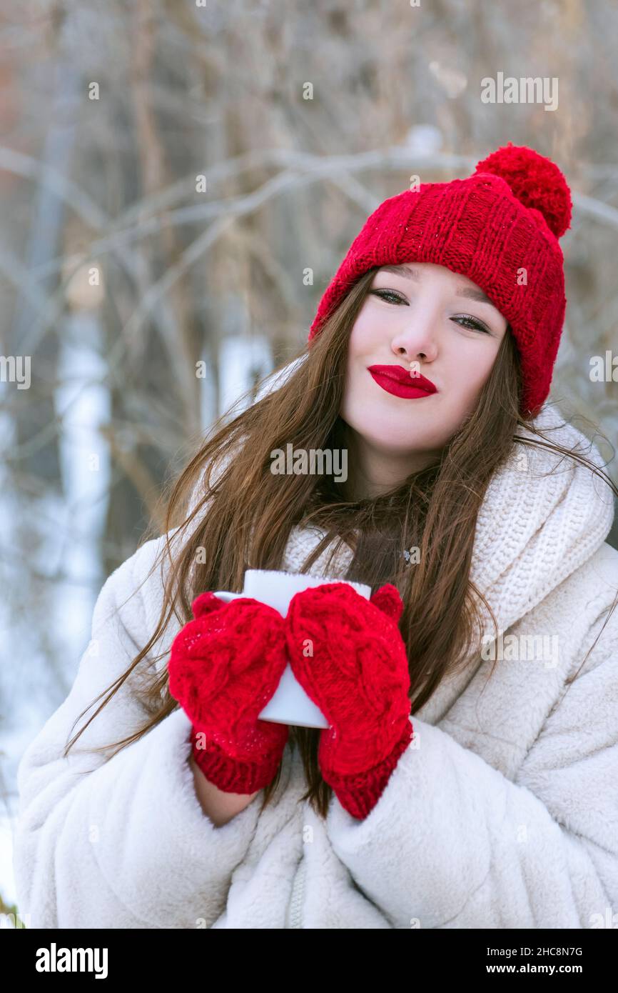 Portrait d'une belle fille en bonnet tricoté rouge et moufles avec une  tasse dans les mains.À l'extérieur.Cadre vertical Photo Stock - Alamy
