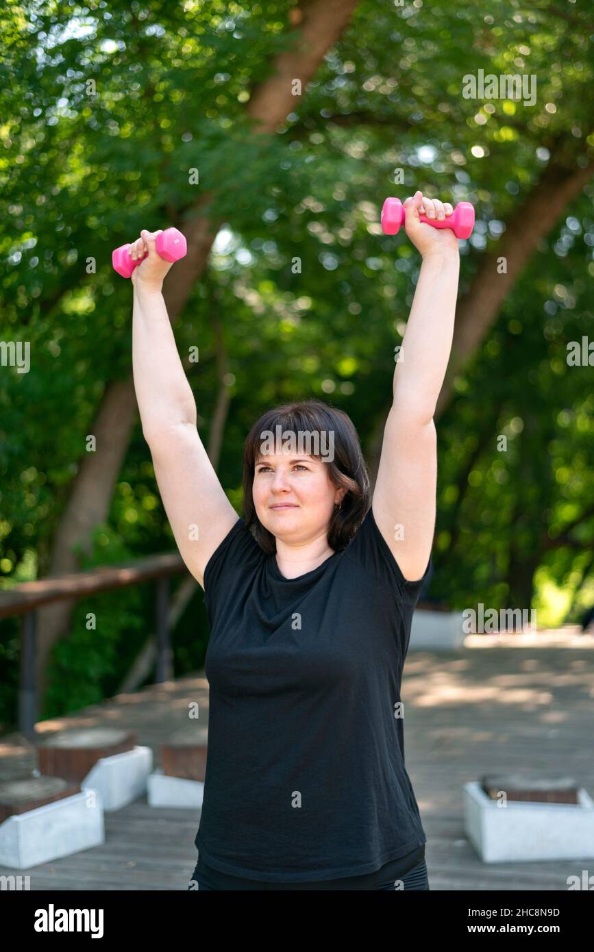 L'entraîneur de fille effectue des exercices avec des haltères dans le parc.Fitness en plein air.Entraînement des mains avec haltères.Pour les débutants.Gros plan. Banque D'Images