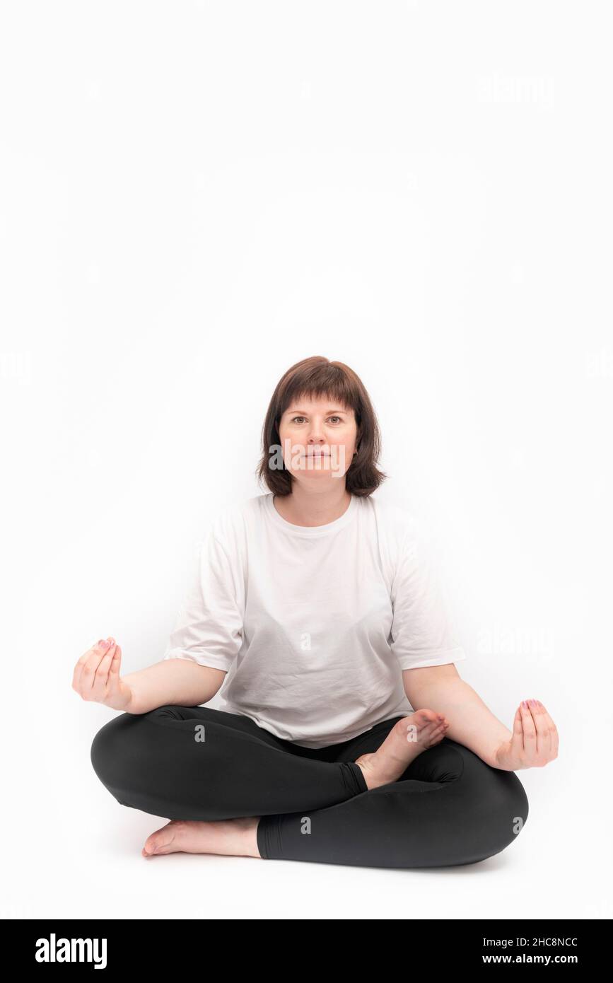 Portrait d'une femme de taille plus de race blanche sur fond blanc pratiquant le yoga.Ardha-Padmasana, demi-pose de lotus.Friteuse verticale.Copier l'espace. Banque D'Images