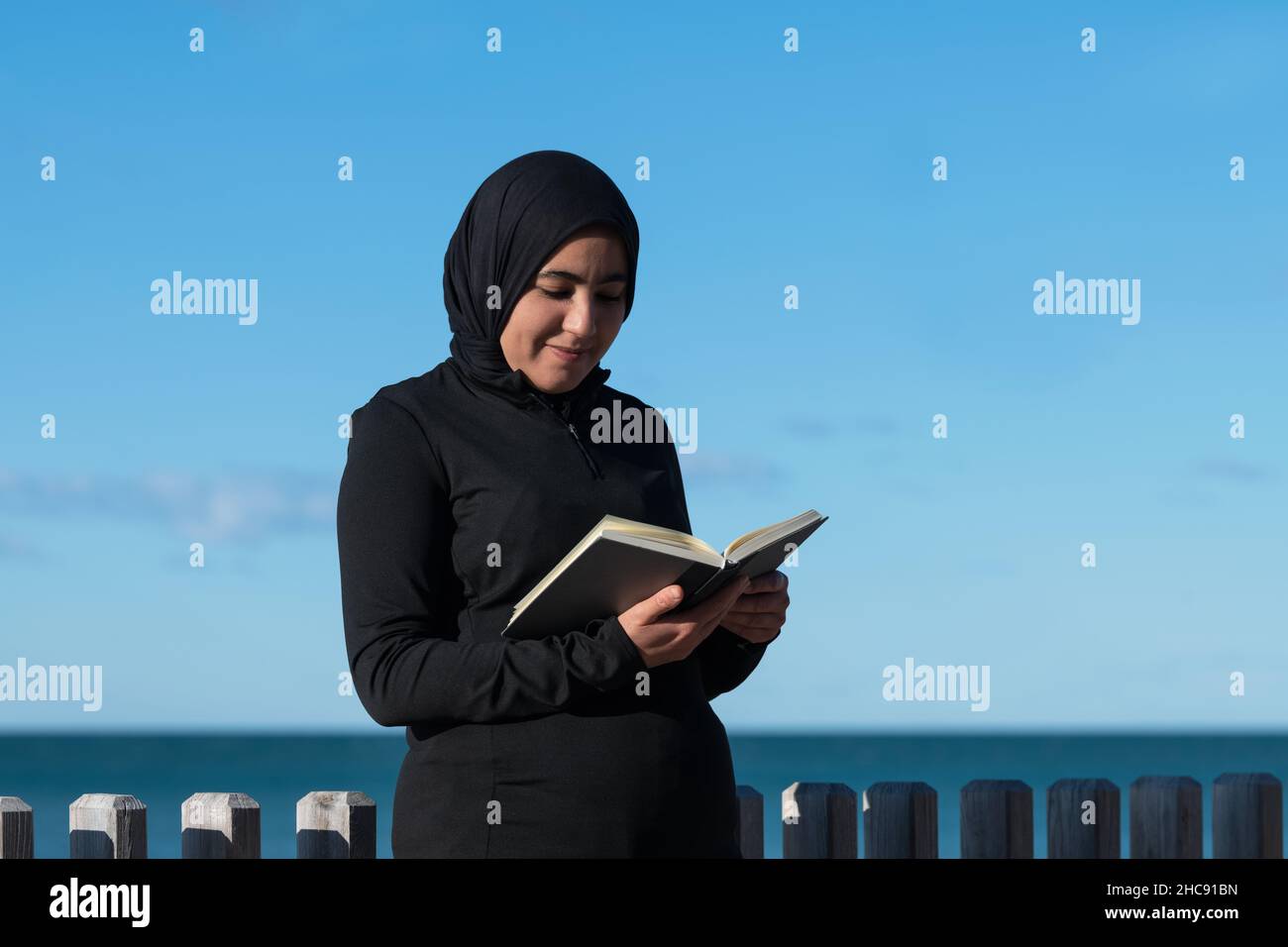 Femme musulmane souriante appréciant un livre à l'extérieur Banque D'Images