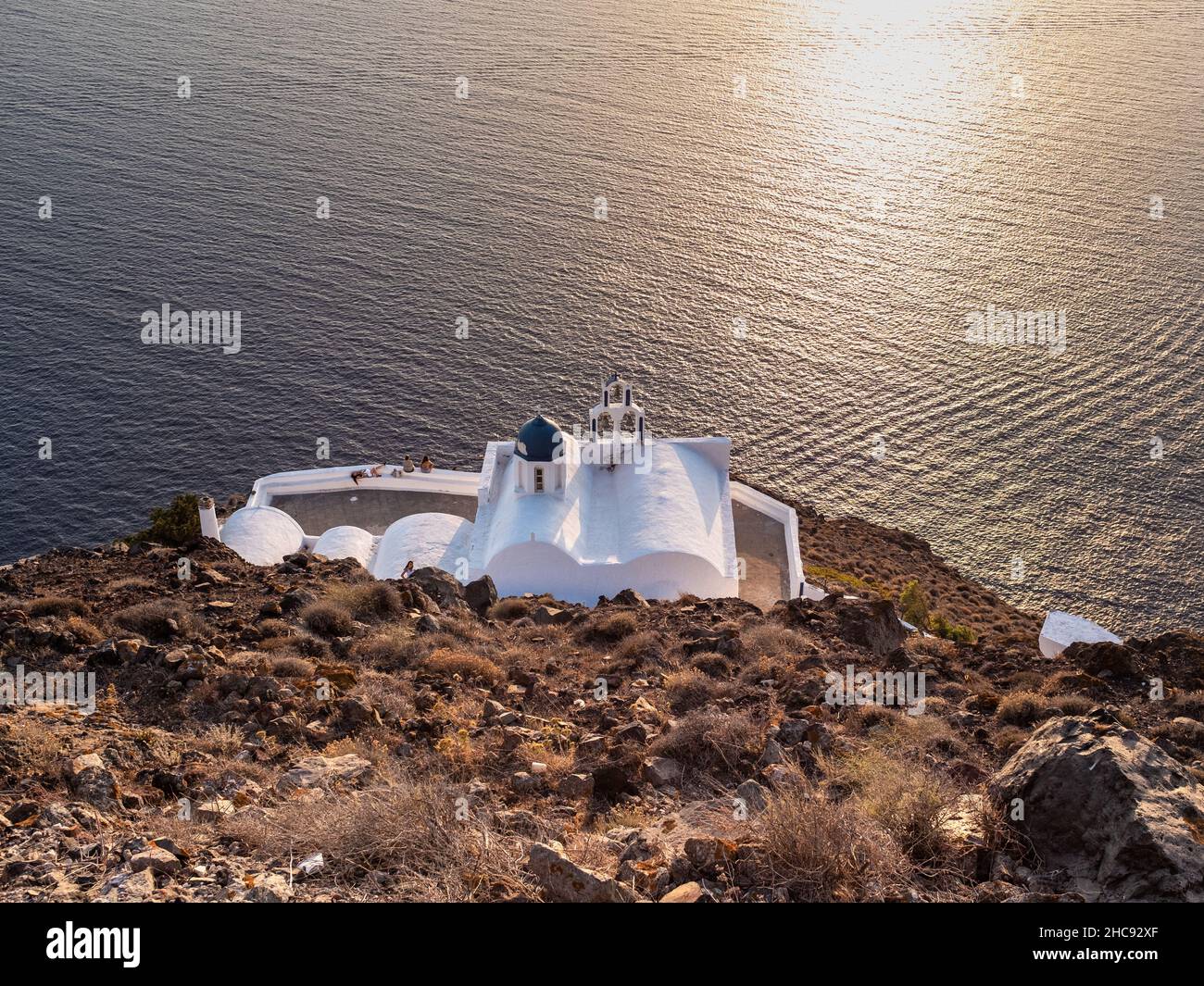 Santorini, Grèce - 28 juillet 2021 : une église orthodoxe grecque typique surplombant la mer Égée avec un reflet ensoleillé sur la surface de la mer.Prise à l'e Banque D'Images