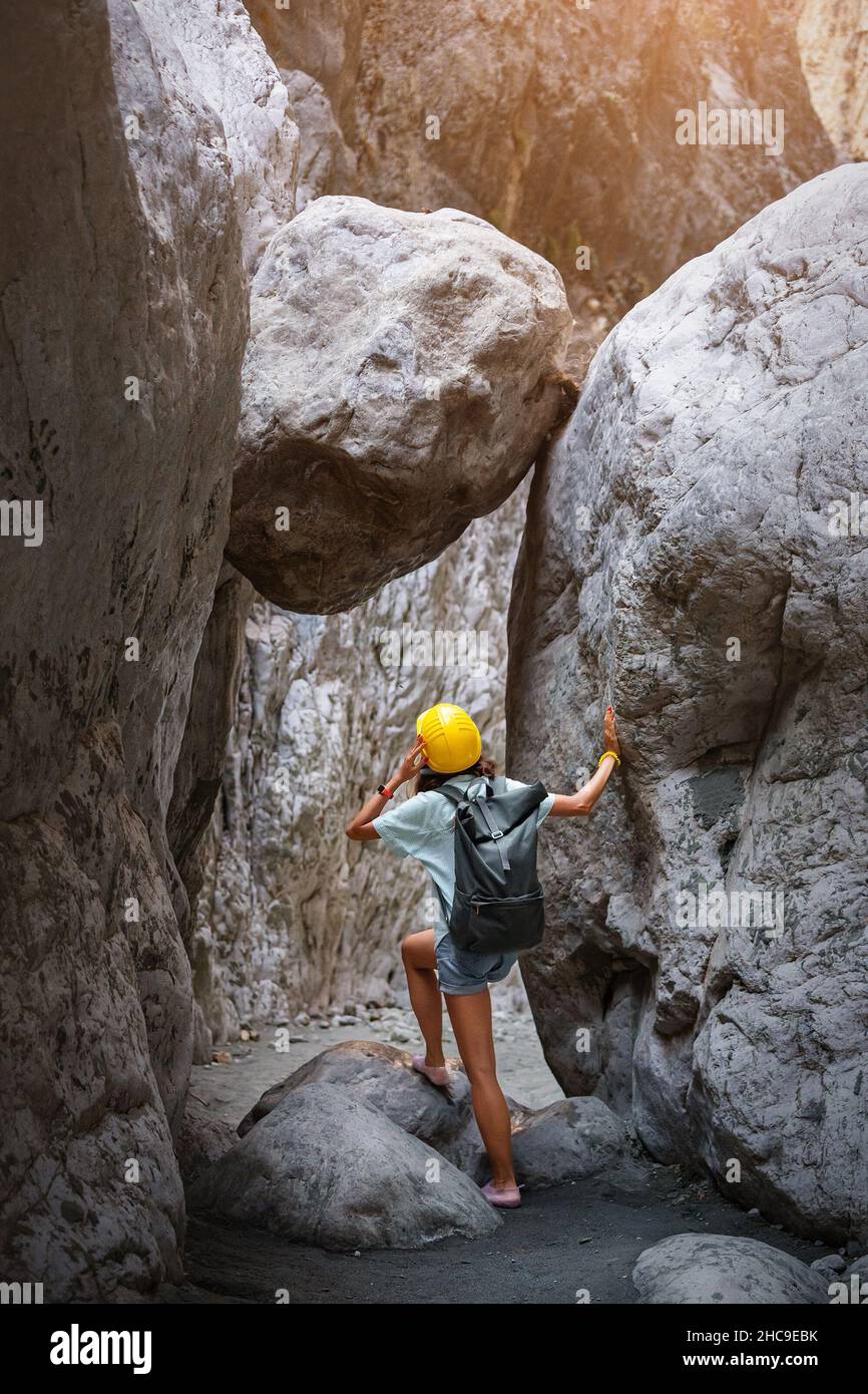 Un aventurier féminin lors d'une randonnée canyoning traverse une gorge étroite sur laquelle pend un énorme rocher.Concept de danger et de chute de roche Banque D'Images
