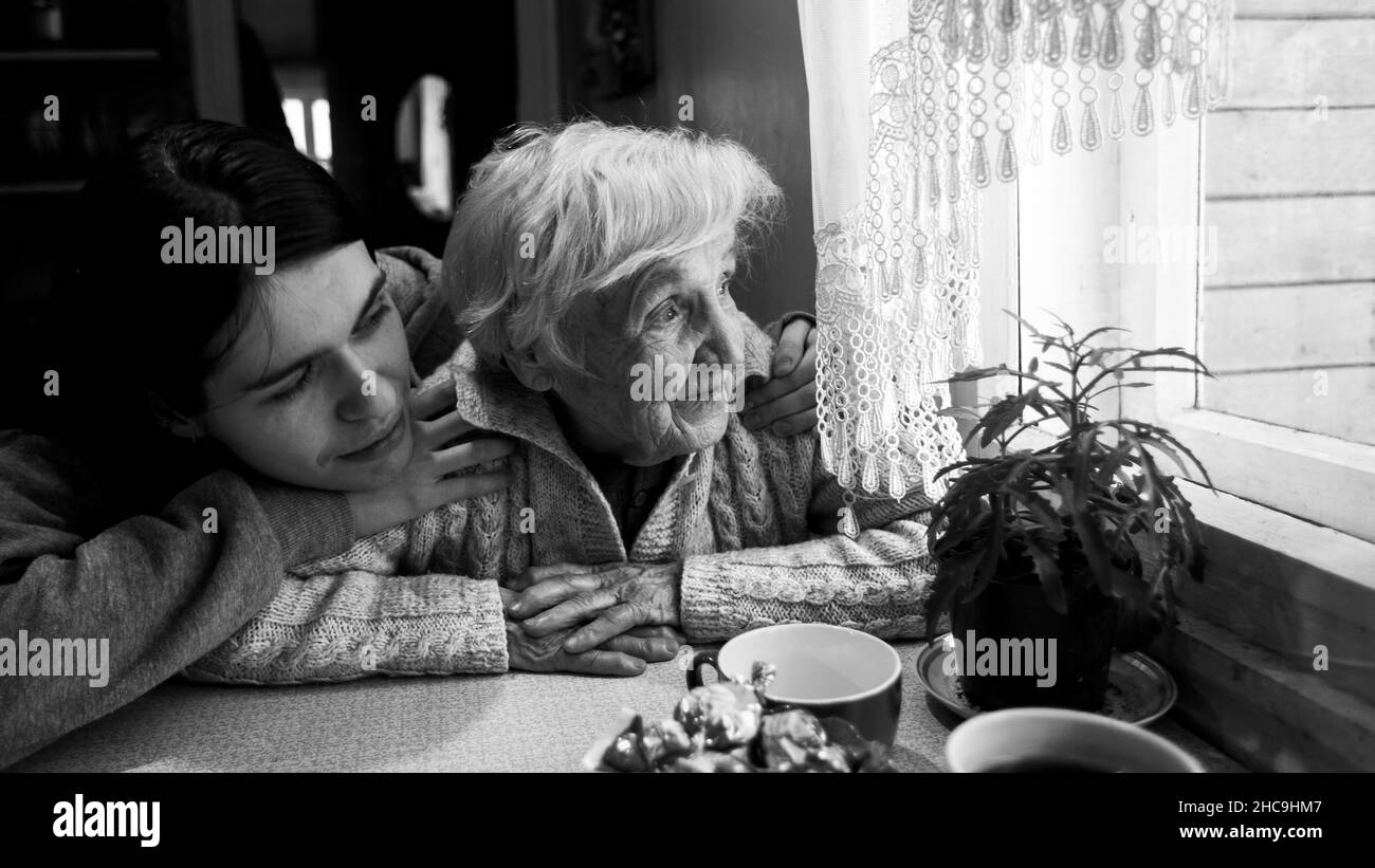 Une femme âgée regarde une fenêtre, avec sa petite-fille adulte, à la maison.Auto-isolation.Photo en noir et blanc. Banque D'Images