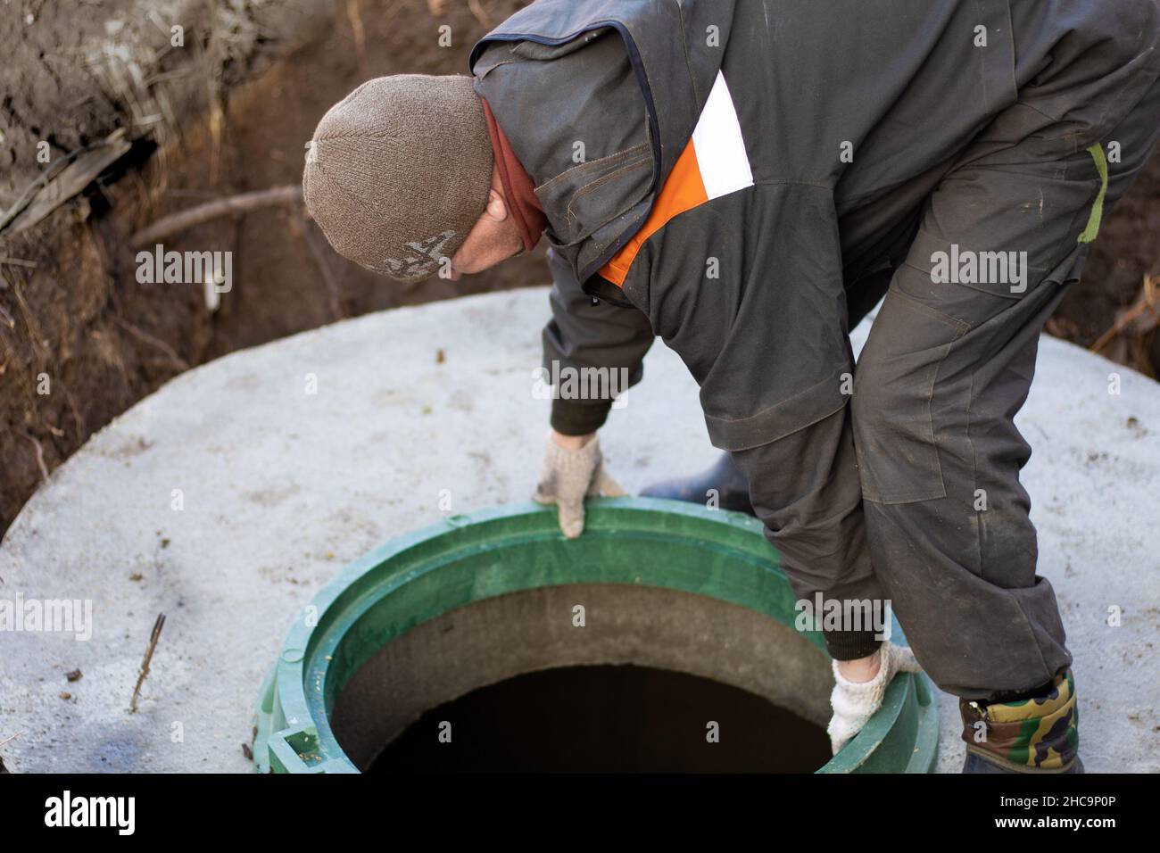 Un homme installe un trou d'égout sur une fosse septique en anneaux de béton.Construction de réseaux d'égouts dans le village. Banque D'Images
