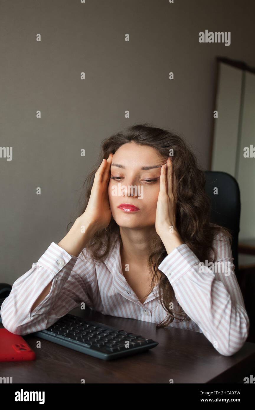 Jeune femme fatiguée avec des cheveux bouclés et une chemise blanche  travaille au bureau avec son ordinateur portable, travail de routine,  freelance, syndrome de l'épuisement Photo Stock - Alamy