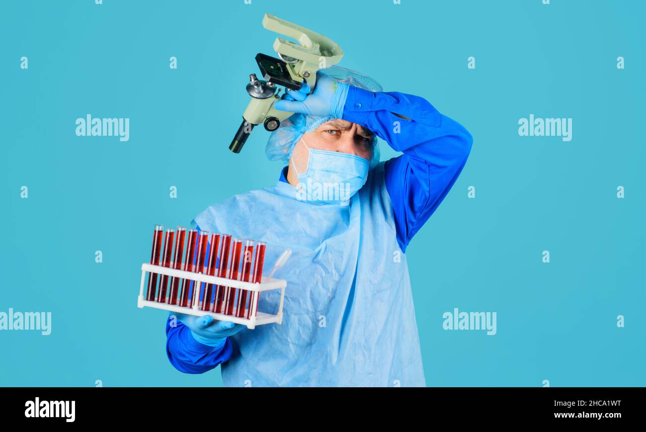 Médecin en masque médical avec échantillon de sang et microscope.Scientifique fatigué avec tubes à essai en laboratoire. Banque D'Images